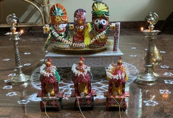 Offering flowers and food to idols of Jagannath, Balabhadra, and Subhadra during a home Rath Yatra puja.